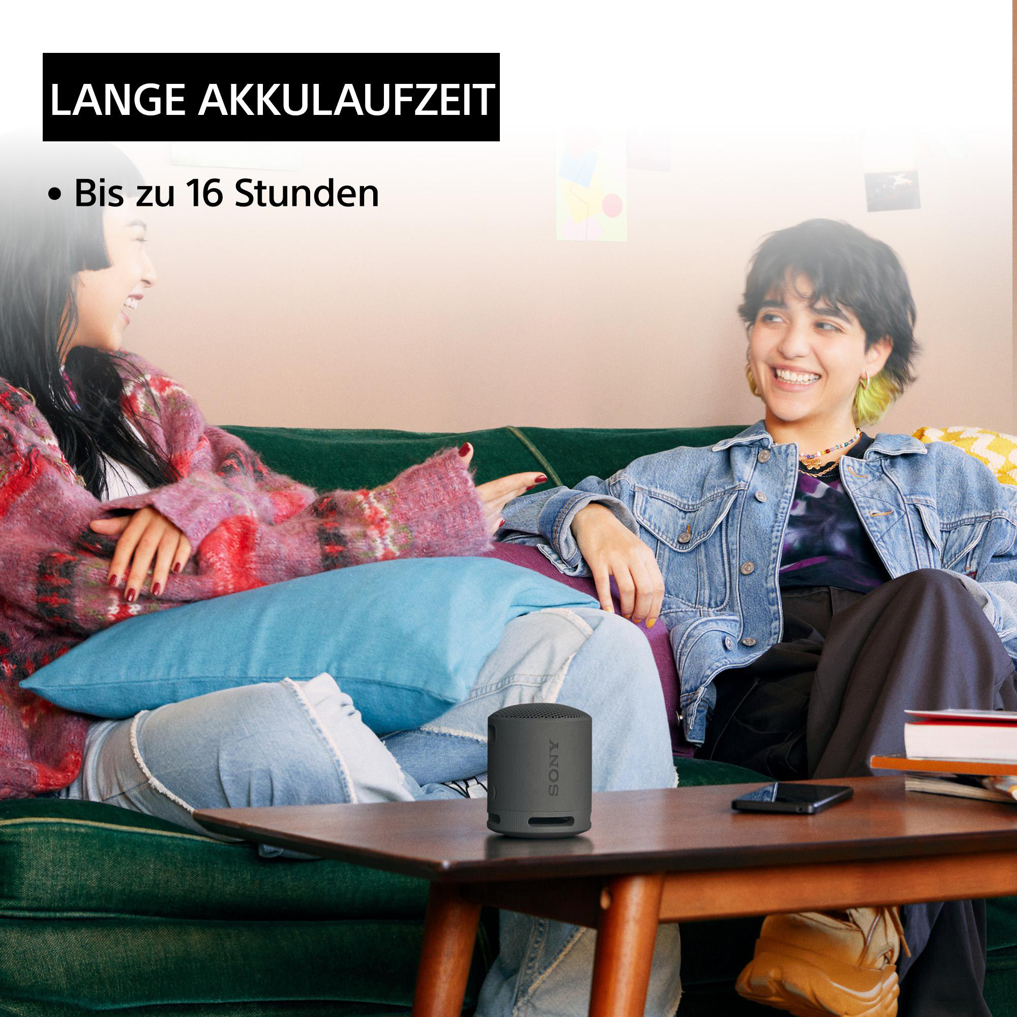 Zwei Personen sitzen auf einem grünen Sofa mit Lautsprecher und Telefon, Text über Akkulaufzeit.