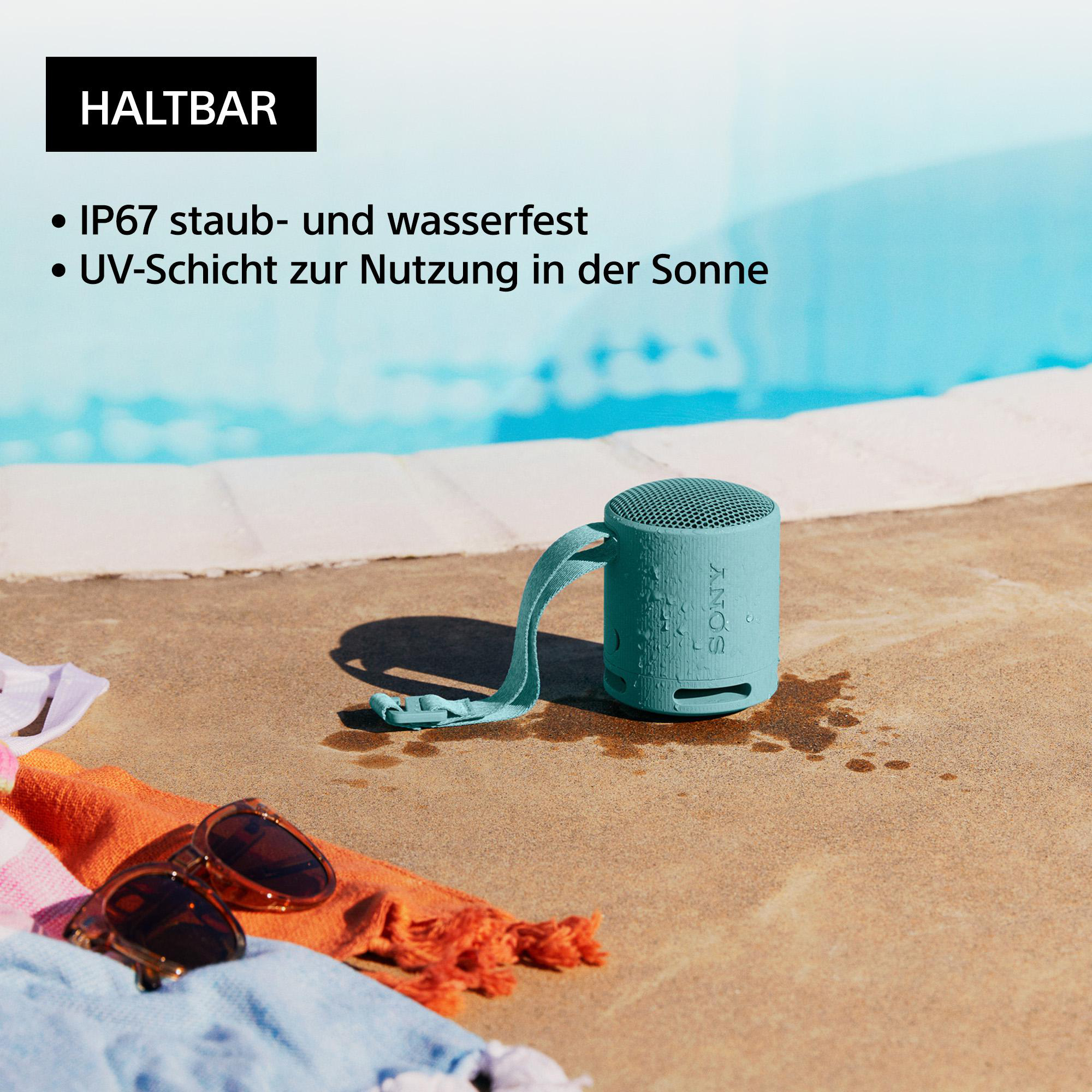 Türkisfarbener tragbarer Lautsprecher in der Nähe eines Pools, mit Sonnenbrille und Handtuch.