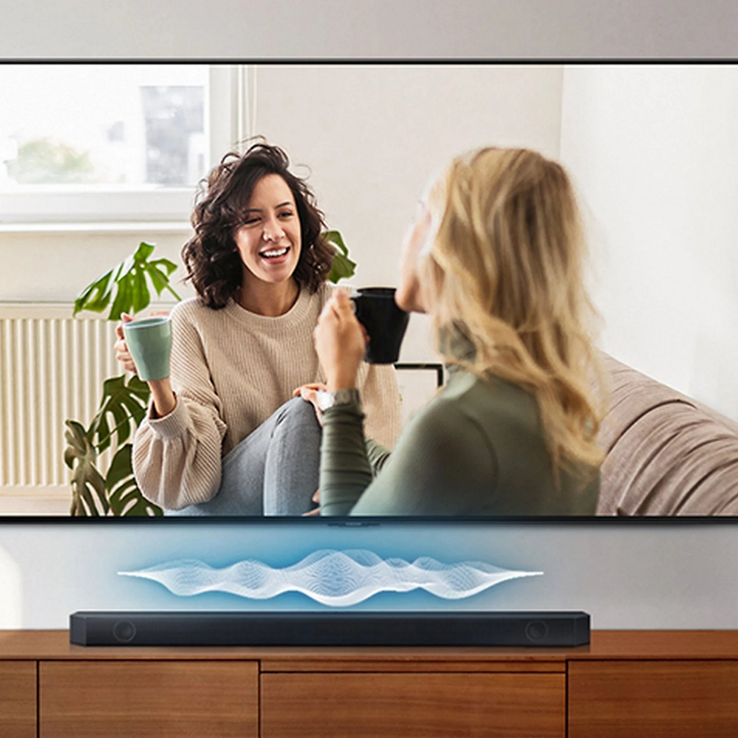 Deux femmes assises, tenant des tasses, regardant la télévision. Une barre de son est en dessous.