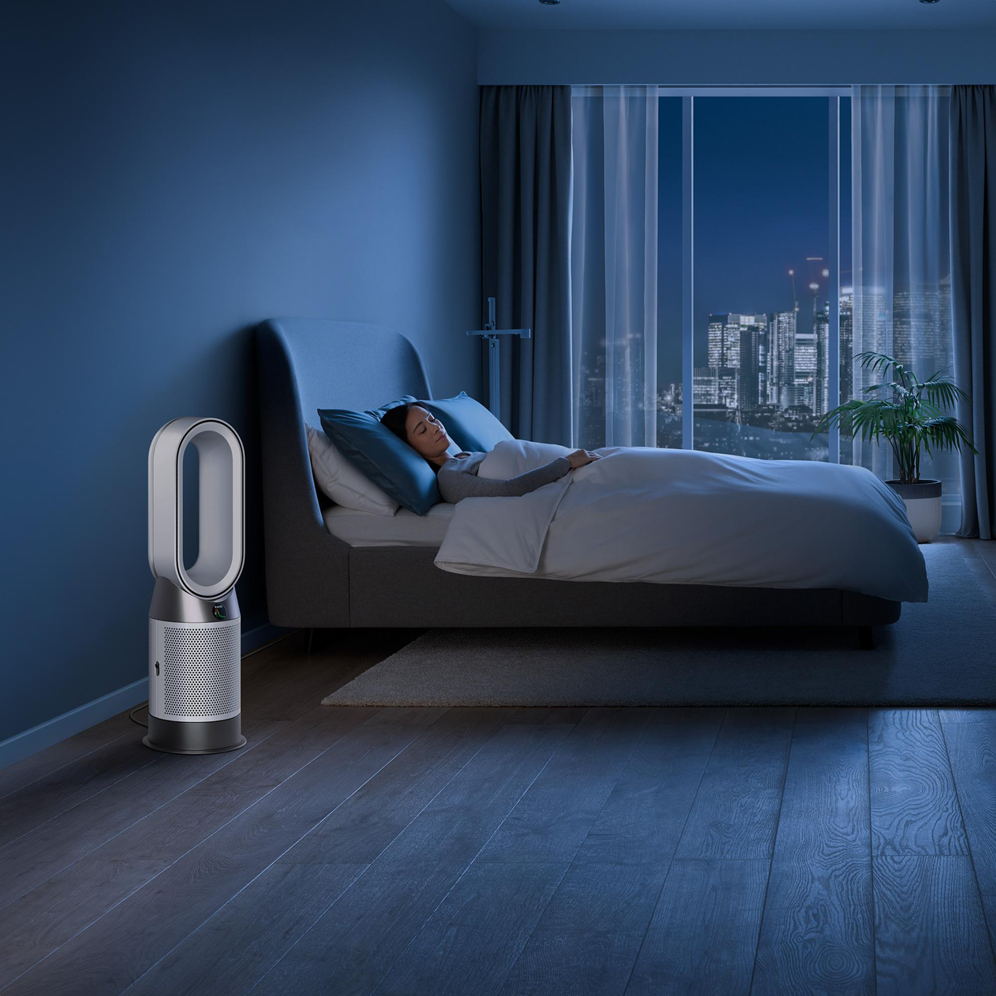 Eine Frau schläft in einem blau getönten Schlafzimmer, mit einem Ventilator neben dem Bett.