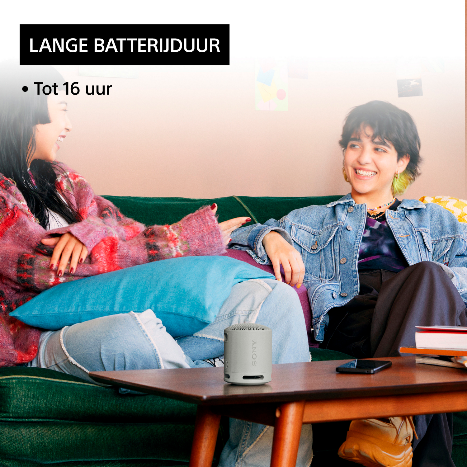 Twee vrouwen op een bank met een luidspreker, de tekst 'LANGE BATTERIJDUUR' staat erboven.