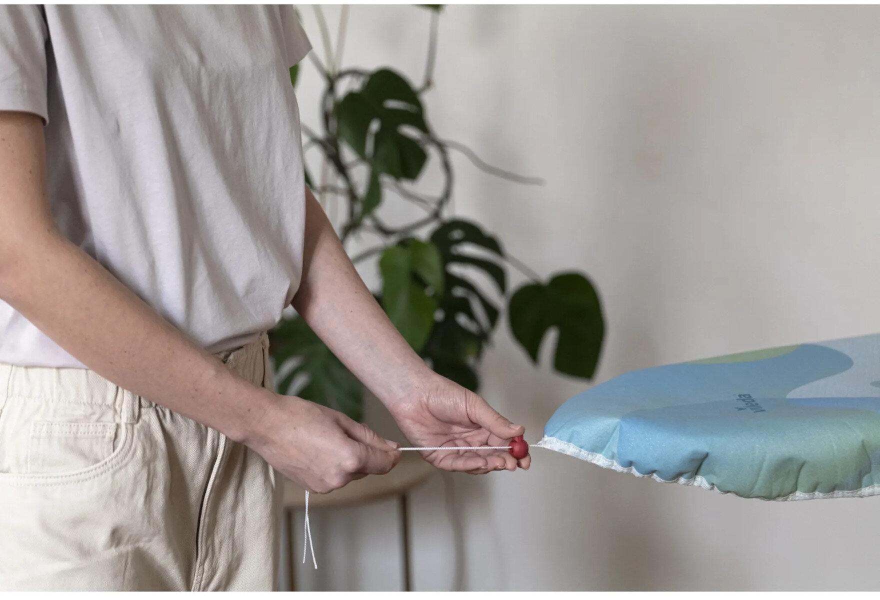 Osoba pociąga za sznurek przymocowany do nadmuchiwanego przedmiotu. Tło to roślina.