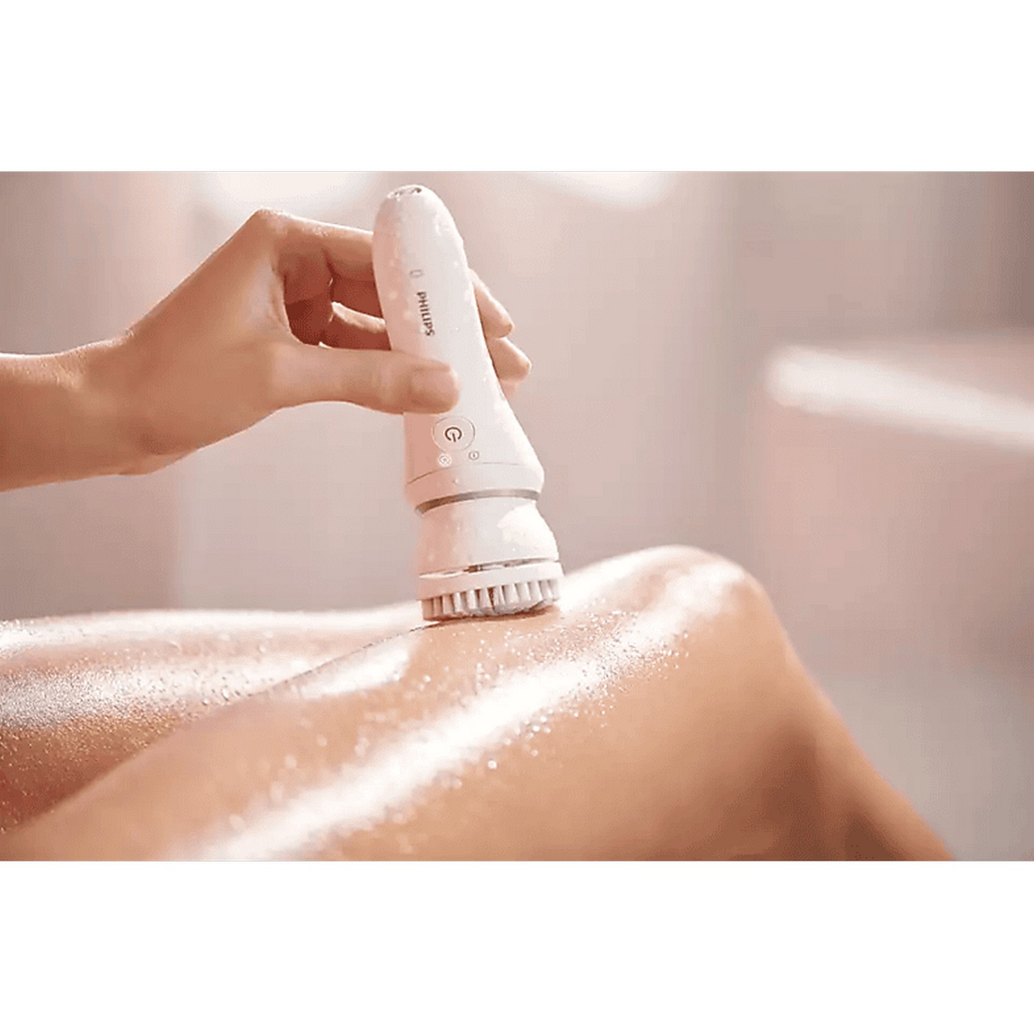 A hand holding a white device on a leg, applying lotion, in a bathroom.