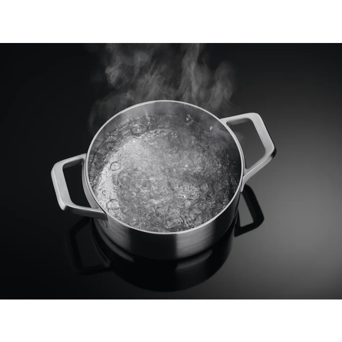 Una olla con agua hirviendo y vapor, sobre una superficie negra.