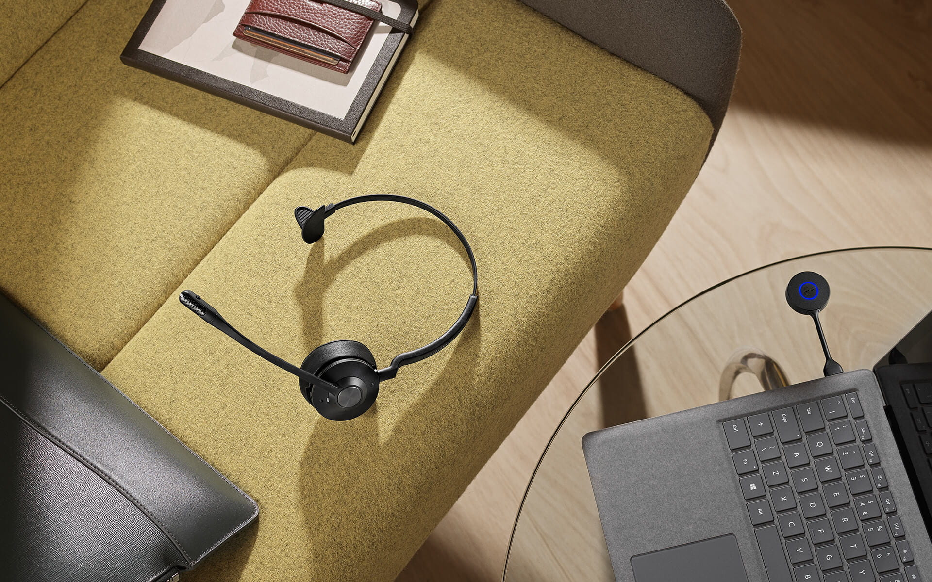 Headset auf einem gelben Sofa, Laptop und andere Gegenstände auf einem Glastisch.