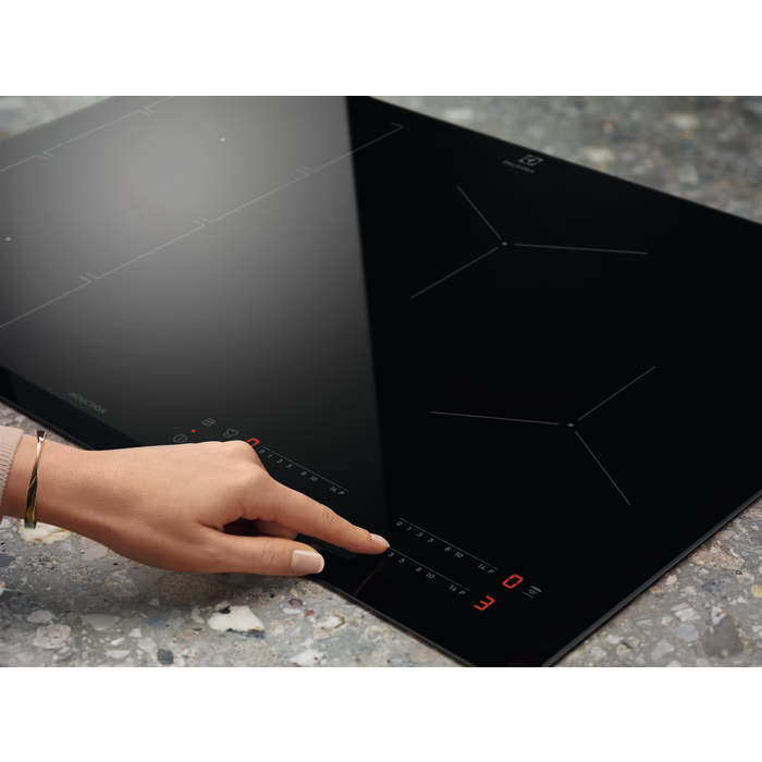 Mano tocando una placa de inducción negra. Pantalla muestra '3'.