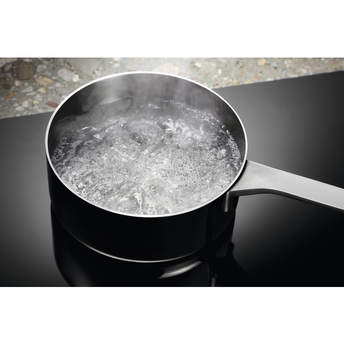 Una olla negra en una estufa negra con agua hirviendo y vapor.