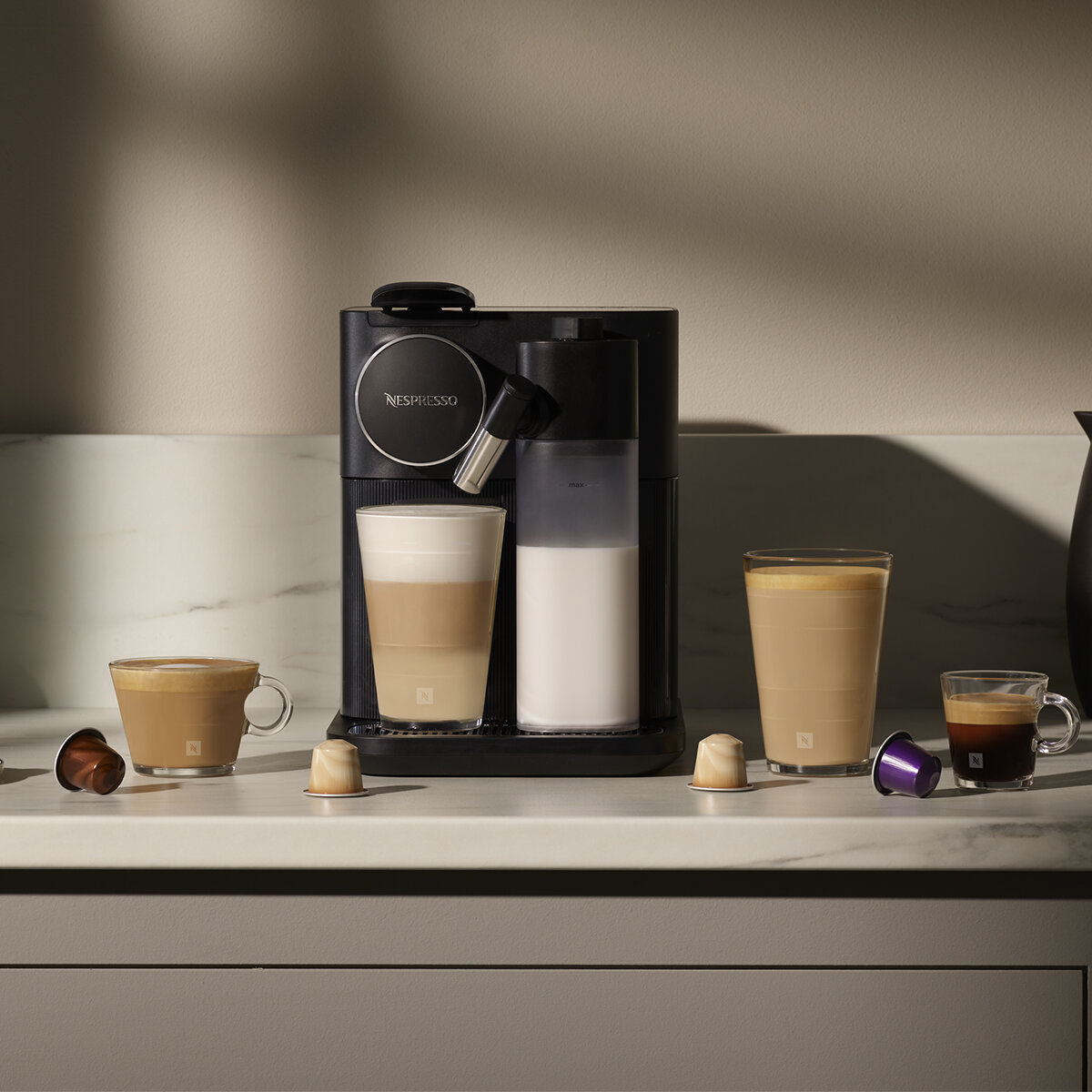 Czarny ekspres do kawy z filiżankami i kapsułkami. Są różne napoje kawowe.