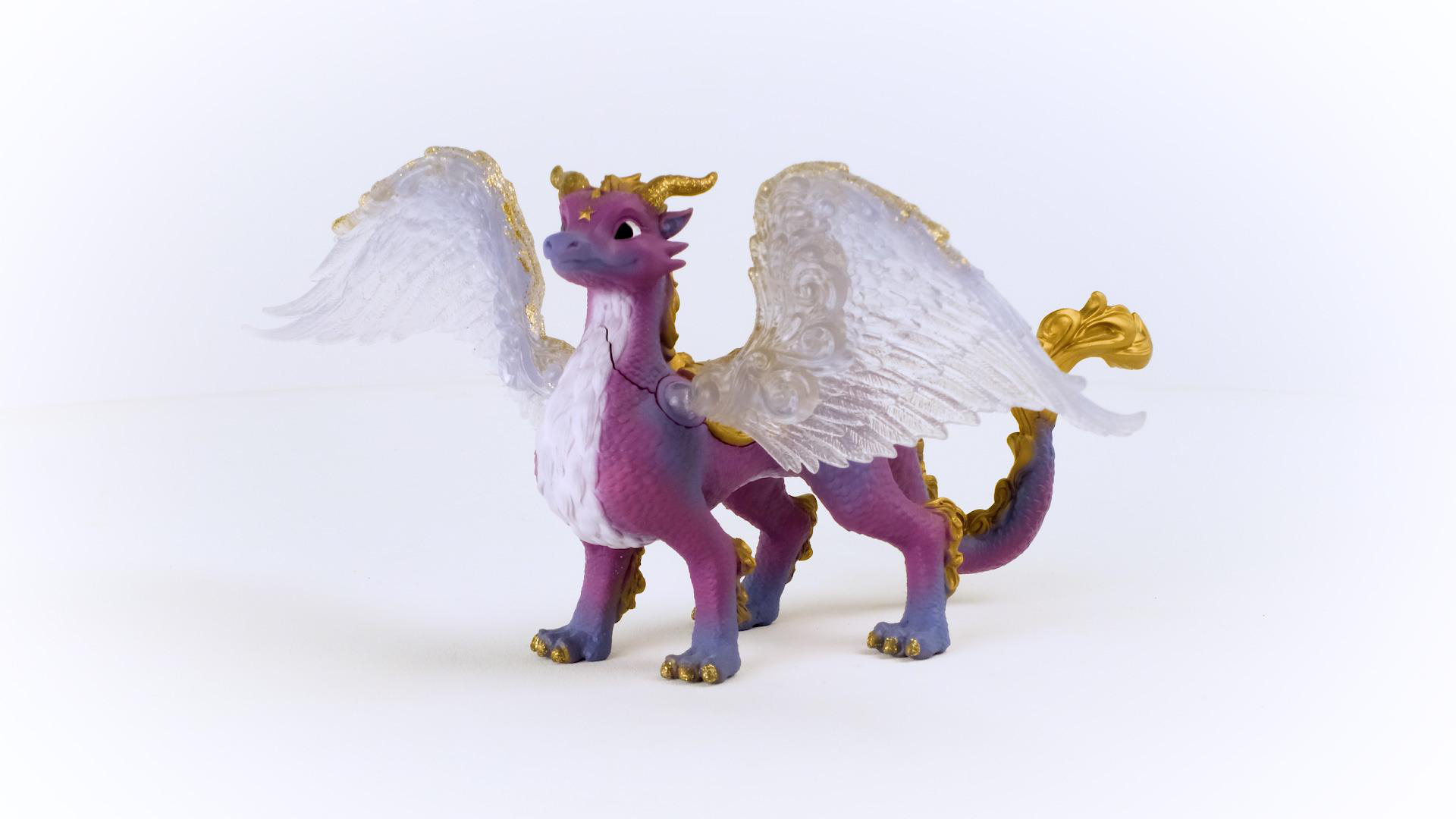 Spielzeugdrache, lila Körper, goldene Hörner und Akzente, weiße Flügel. Steht auf weißer Oberfläche.