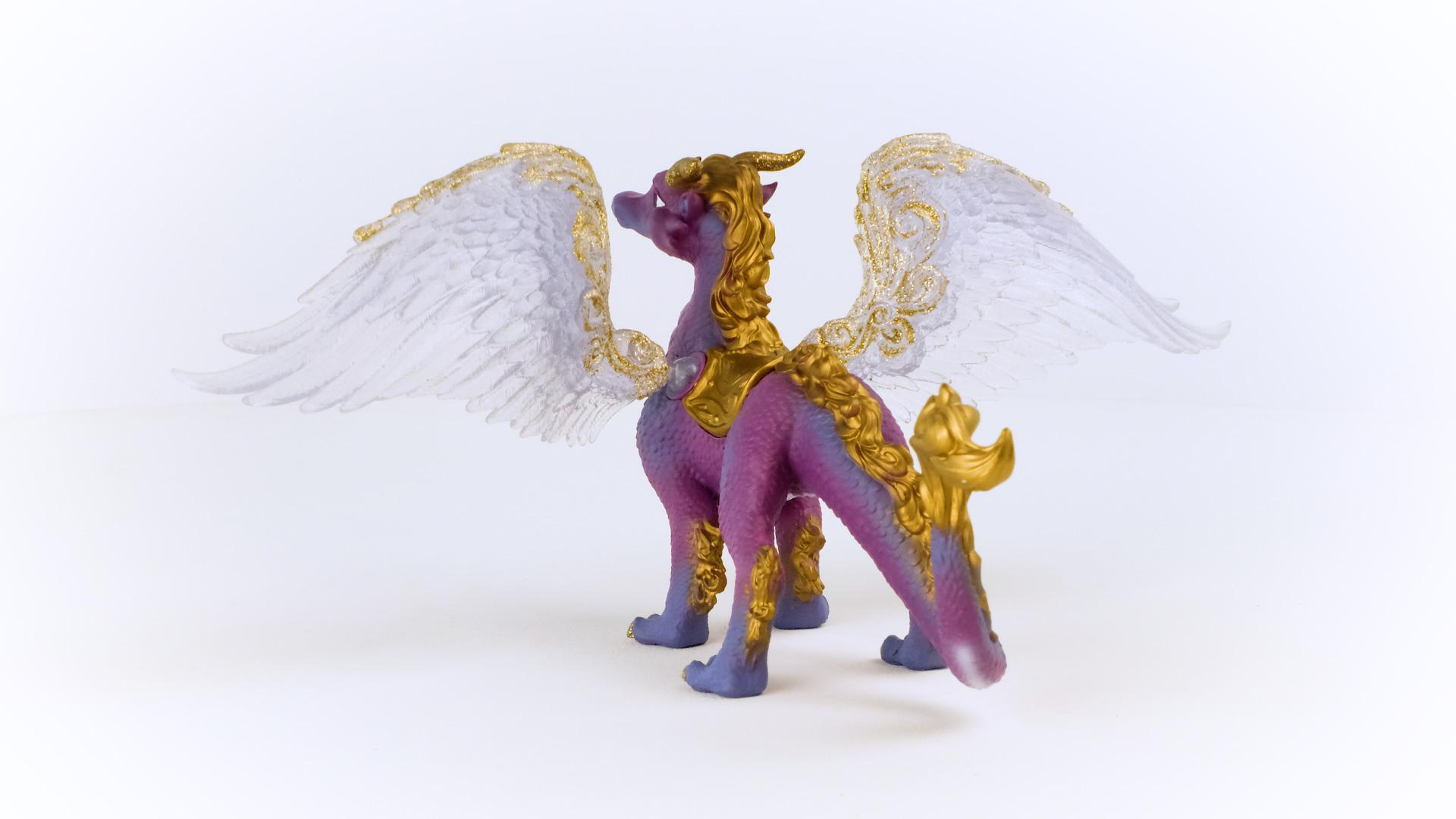 Eine lila und goldene Drachenfigur mit transparenten Flügeln, die auf einer weißen Oberfläche steht.