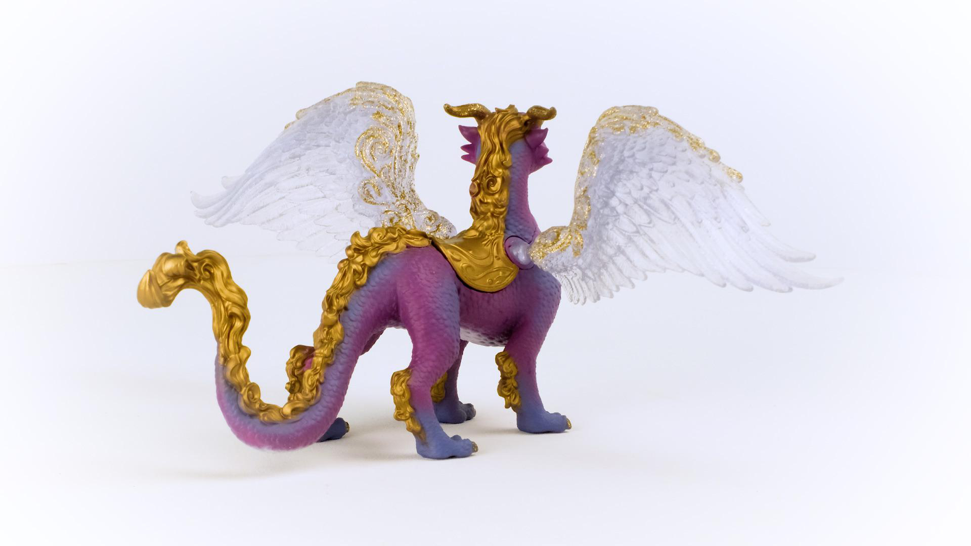 Lila Drachenfigur mit goldenen Akzenten, weißen Flügeln, auf weißer Oberfläche stehend. Seitenansicht.