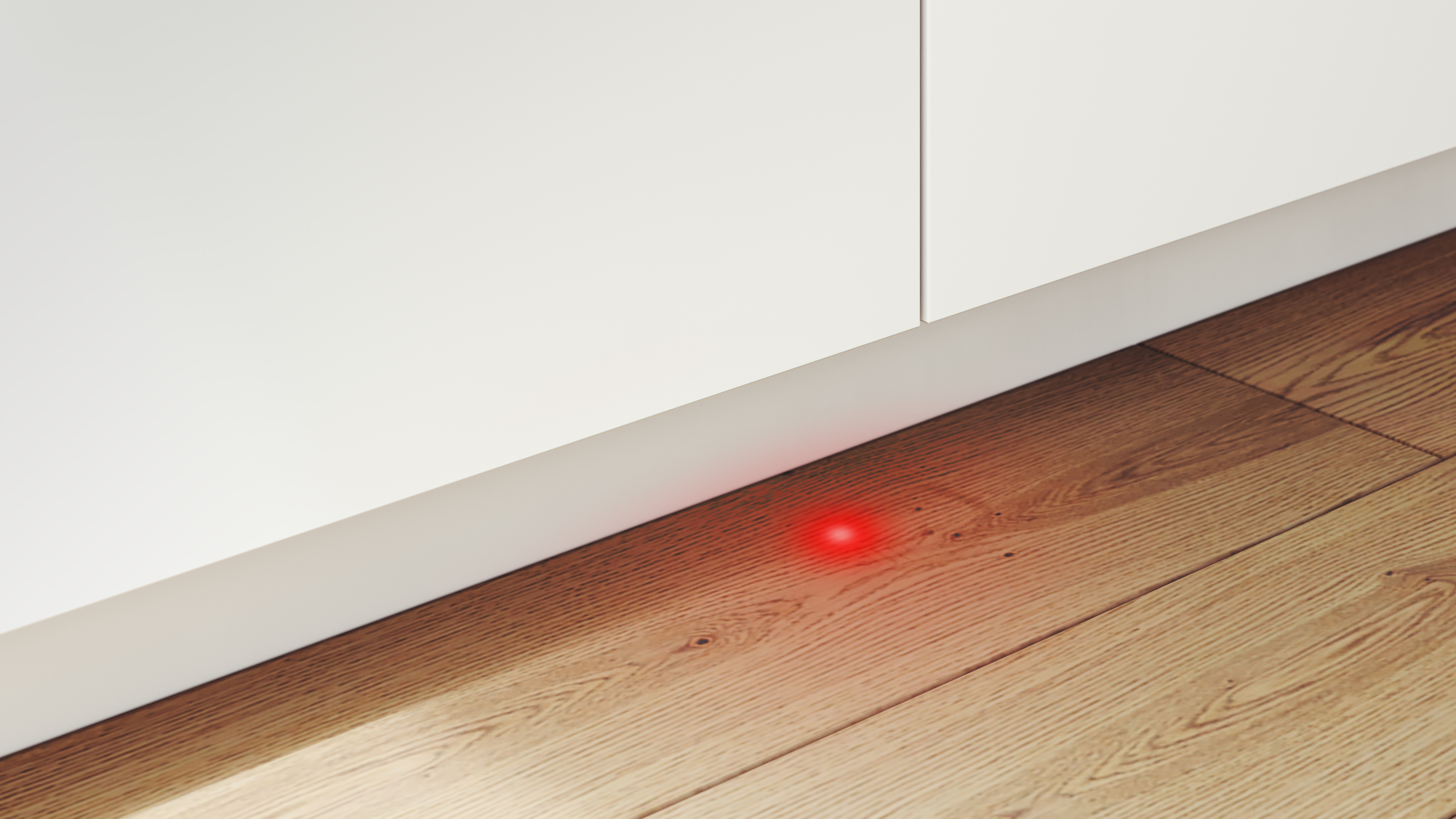 Ein rotes Licht, das unter einem weißen Schrank auf einem Holzboden leuchtet.