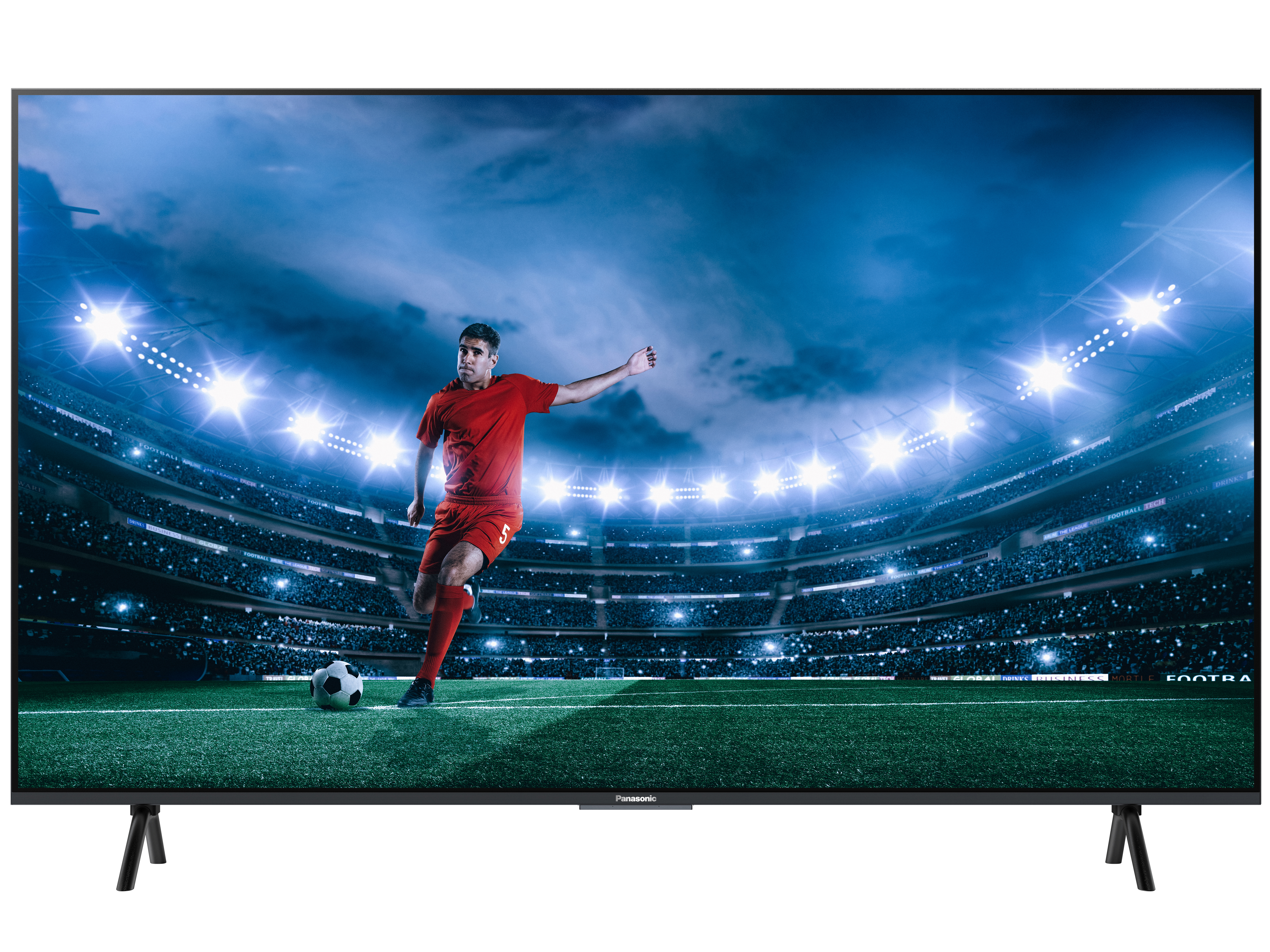 Ein Fernseher zeigt ein Fußballspiel. Ein Spieler in Rot schießt einen Ball auf einem grünen Feld. Stadion im Hintergrund.
