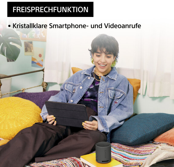Lächelnde Frau, die ein Tablet benutzt, mit Lautsprecher auf dem Tisch vor ihr.