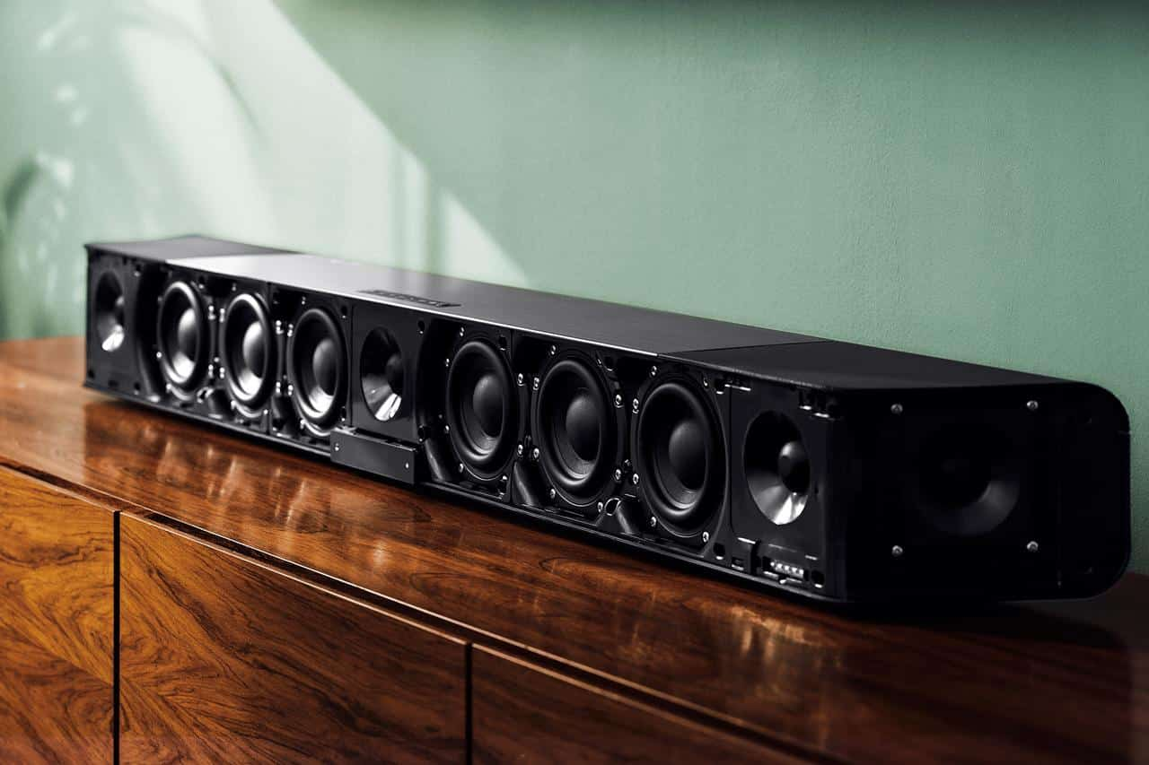 Fekete soundbar egy fa szekrényen, több hangszóróval.