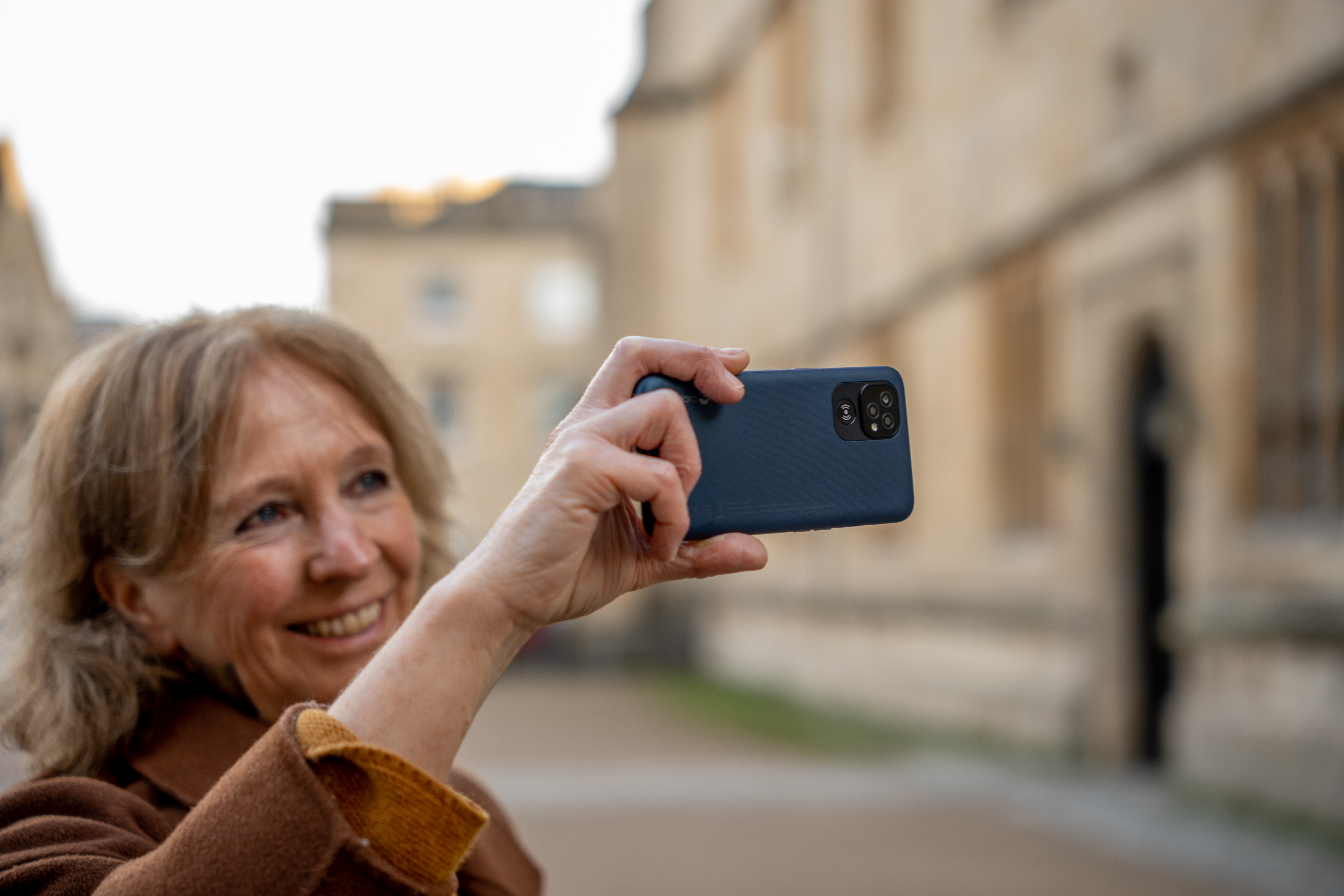 Une femme prend un selfie avec un téléphone, dans une rue avec de vieux bâtiments.