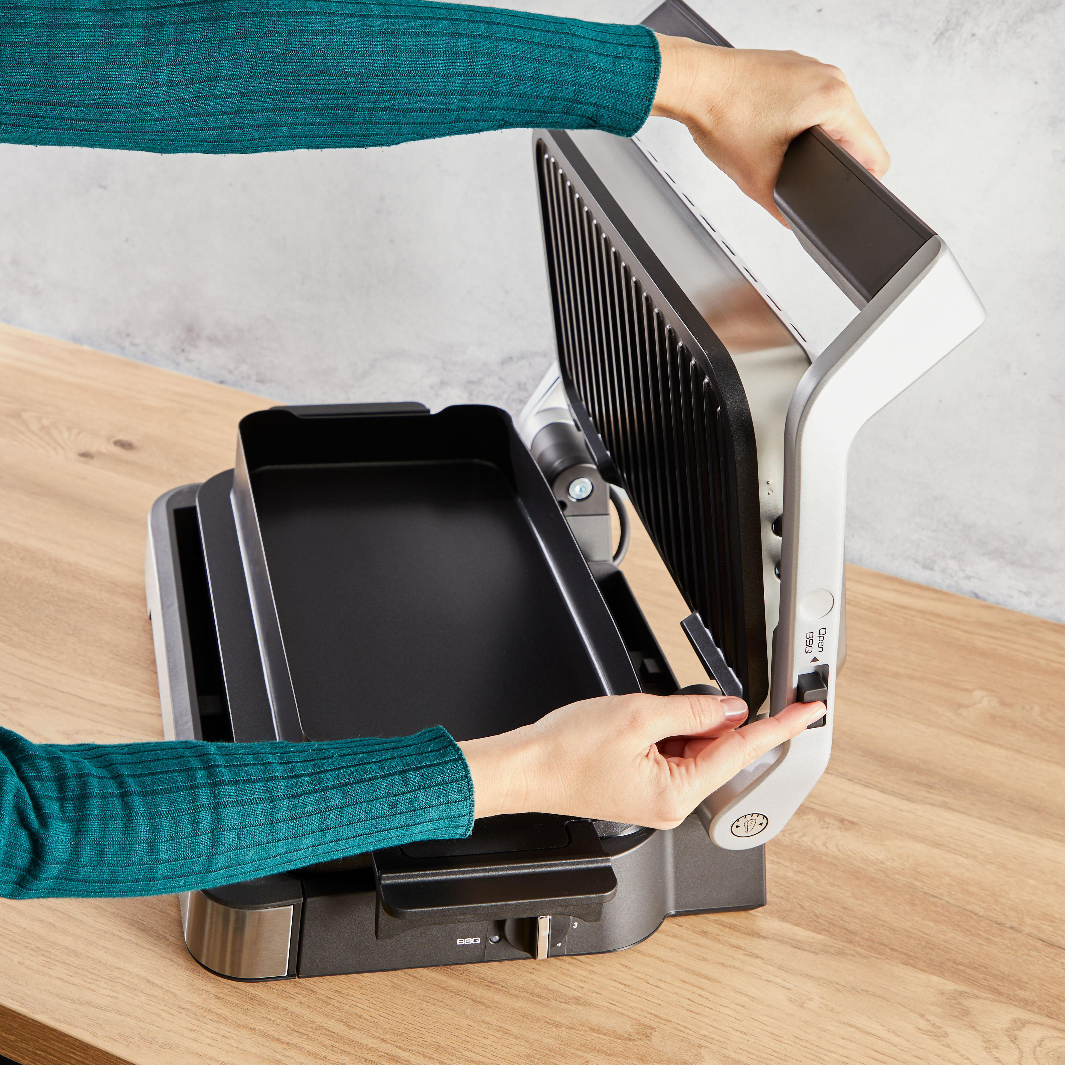 Hände, die einen Grill bedienen. Der Grill ist offen, mit einer schwarzen Kochfläche.