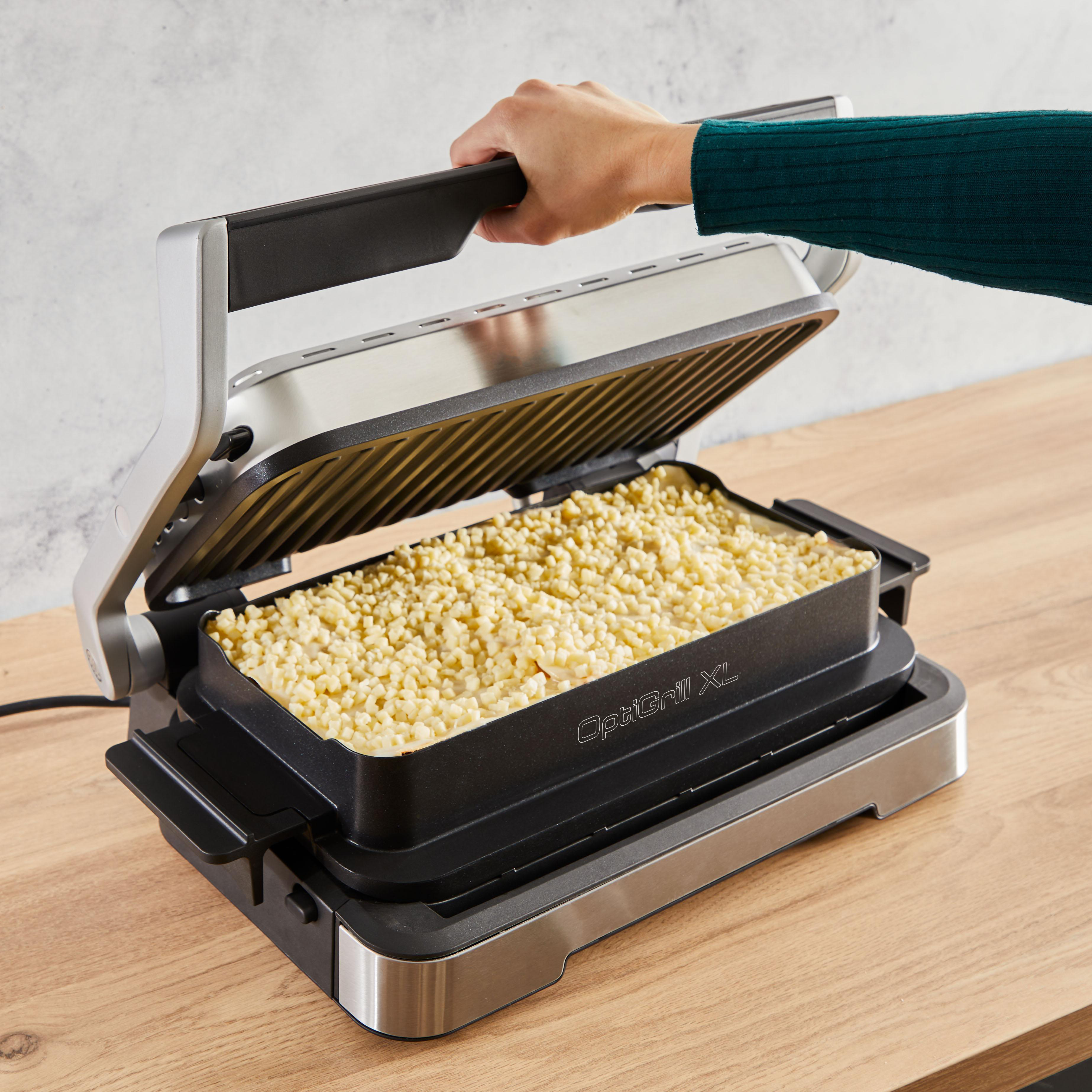 Grill mit Essen, eine Hand öffnet ihn. Der OptiGrill XL steht auf einer Holzoberfläche.