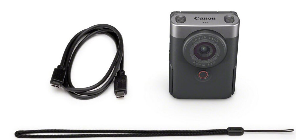 Aparat z obiektywem, kablem USB i paskiem na nadgarstek na białym tle.