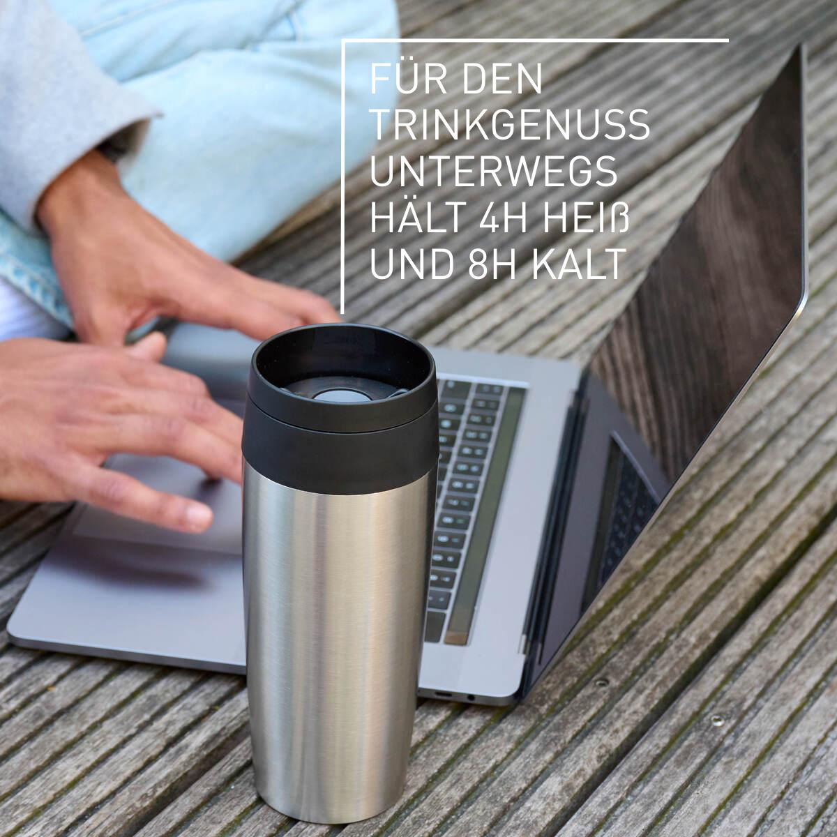 Eine Person benutzt einen Laptop neben einer Thermoskanne auf Holzplanken.