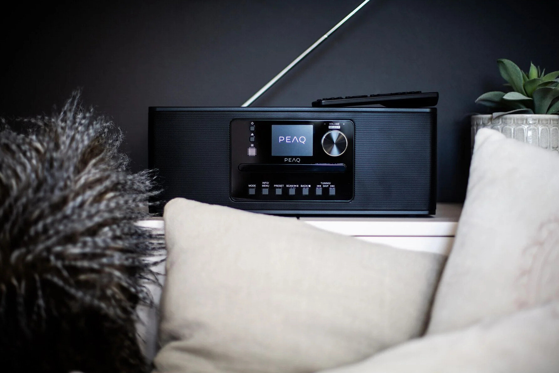 Czarny radioodbiornik na białej powierzchni, z pilotem i ozdobnymi poduszkami.