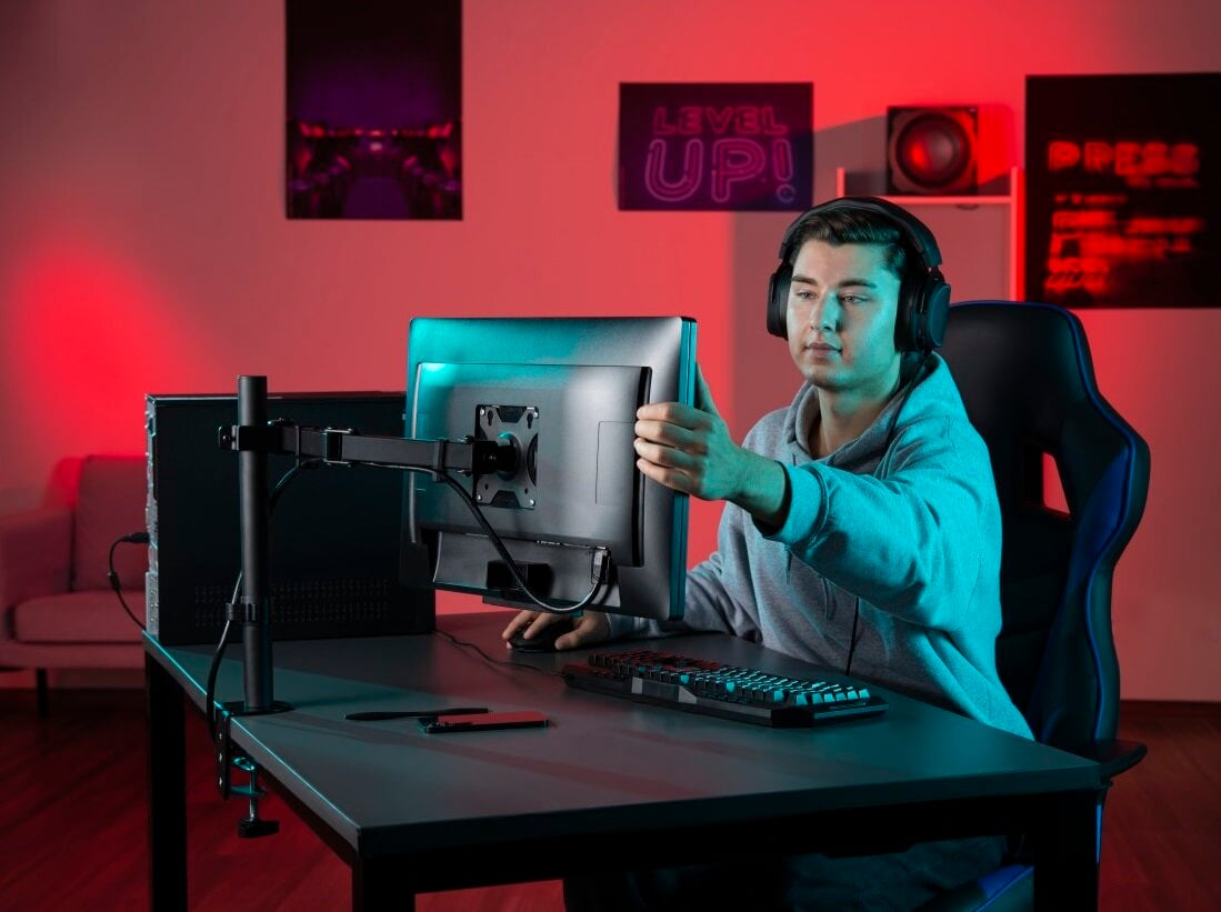 Gracz reguluje monitor na biurku ze światłami i akcesoriami do gier.