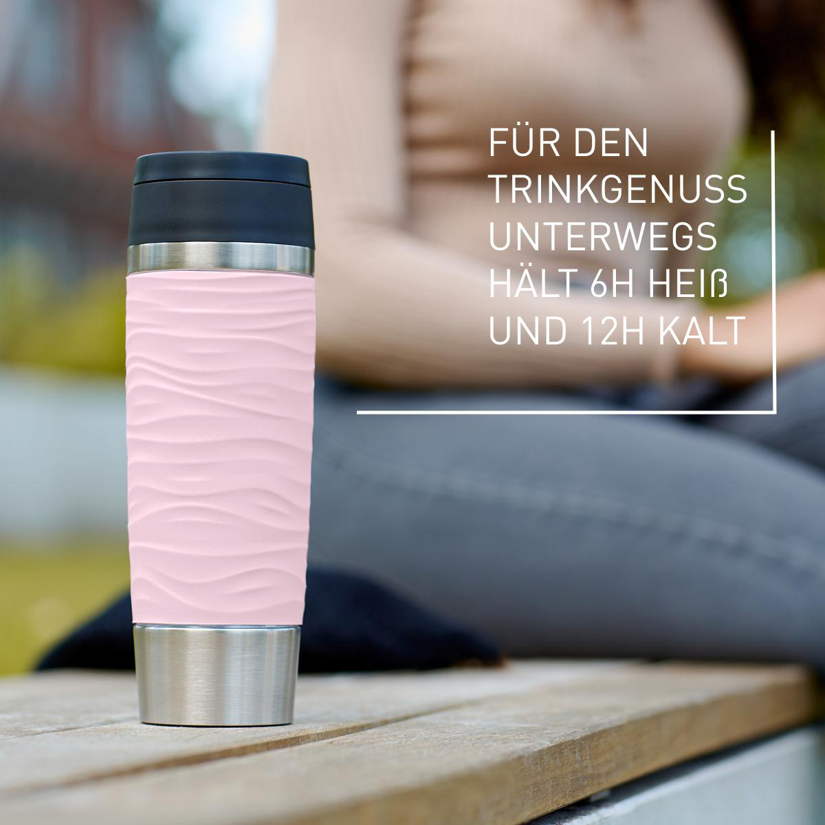 Ein rosa Reisebecher mit Wellenmuster und schwarzem Deckel, der auf einer Oberfläche steht.