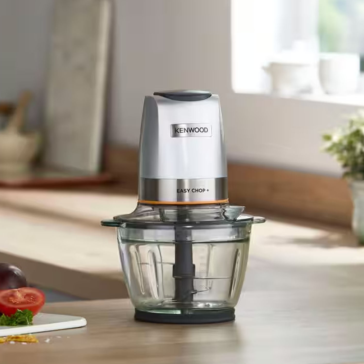 Robot da cucina argento e nero su una superficie in legno. Sono presenti una ciotola di vetro e un pomodoro.