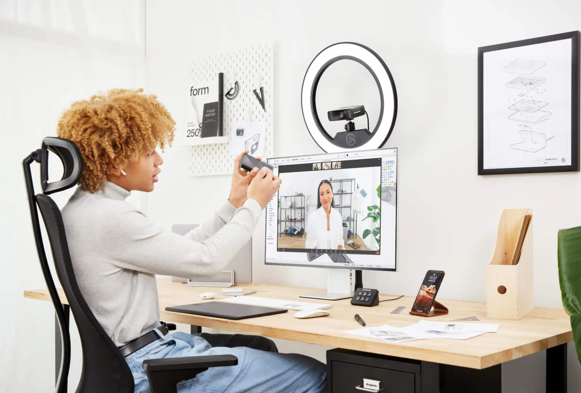 Une personne dans un bureau à domicile configure un appel vidéo avec un anneau lumineux et un moniteur.