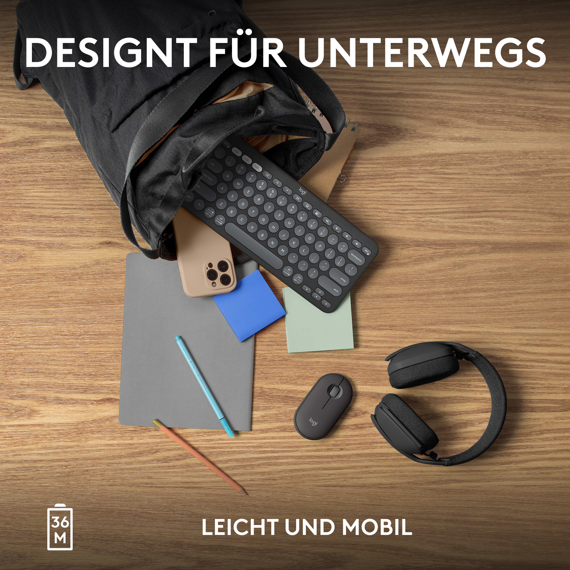 Eine schwarze Tragetasche mit Gegenständen: Tastatur, Telefon, Notizblock, Stift, Maus und Kopfhörer auf Holztisch.