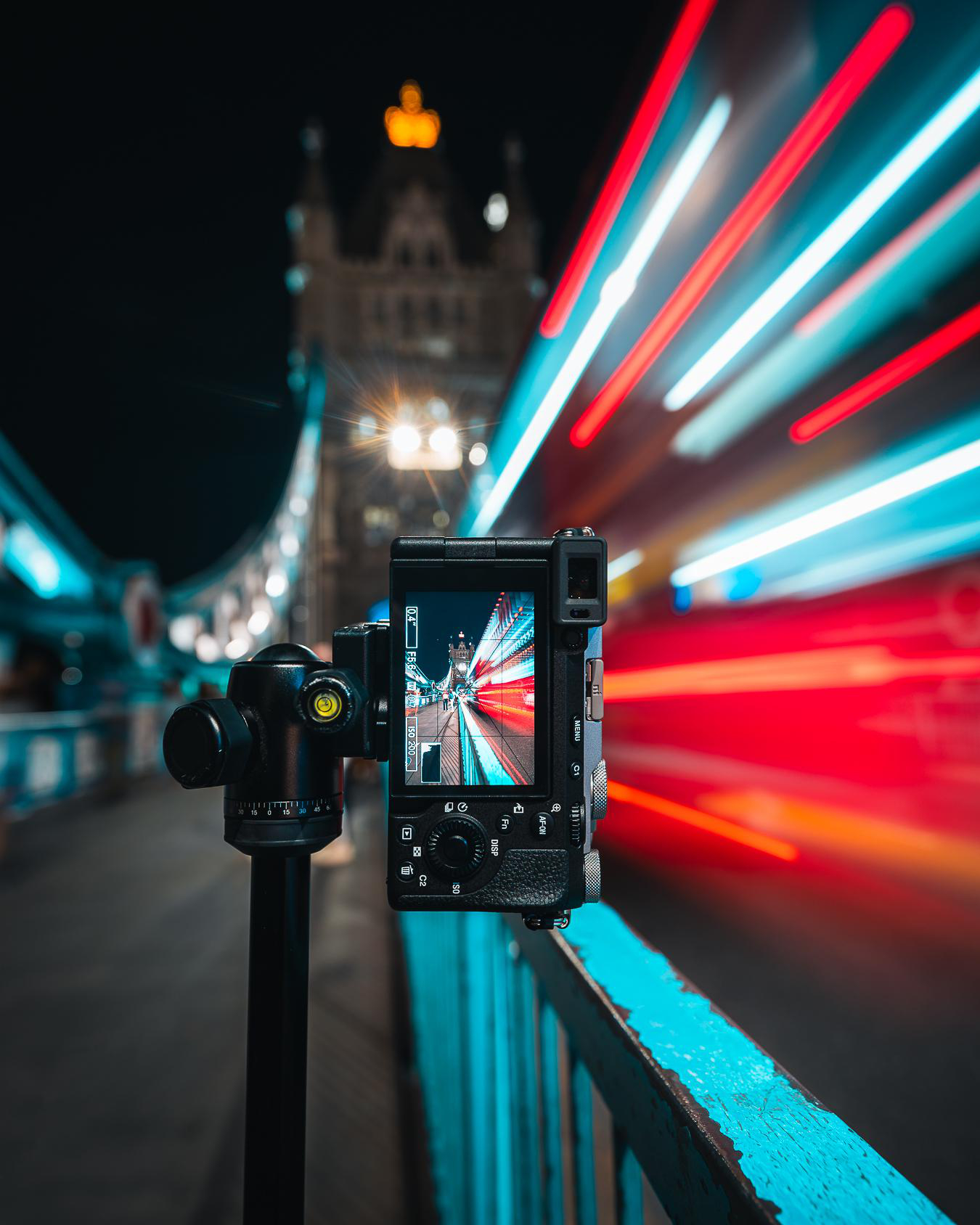 Kamera auf Stativ, filmt die Tower Bridge in London bei Nacht, mit Lichtspuren. Blaue und rote Lichter.