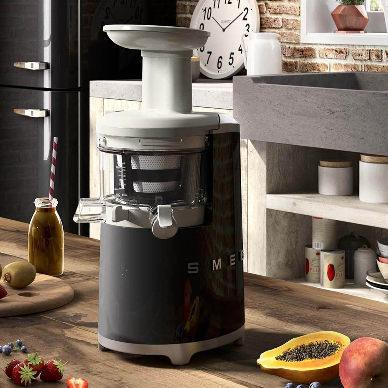 Un estrattore di succo con base grigio scuro e parte superiore bianca, con vari frutti intorno.