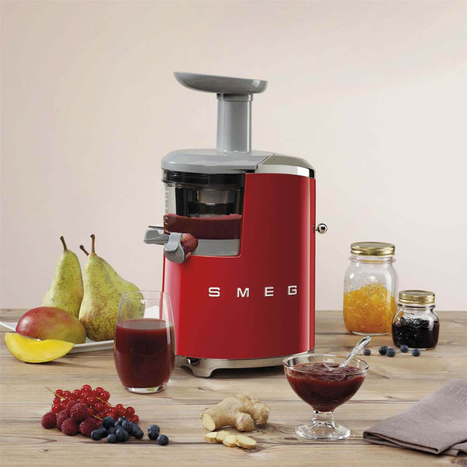 Estrattore di succo SMEG rosso con frutta e bicchieri di succo, tra cui pere, mango e bacche su legno.