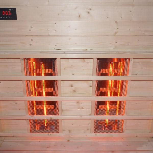 Innenraum einer Sauna. Holzwände und Bänke. Zwei Infrarot-Heizungen mit leuchtenden Lichtern sind sichtbar.