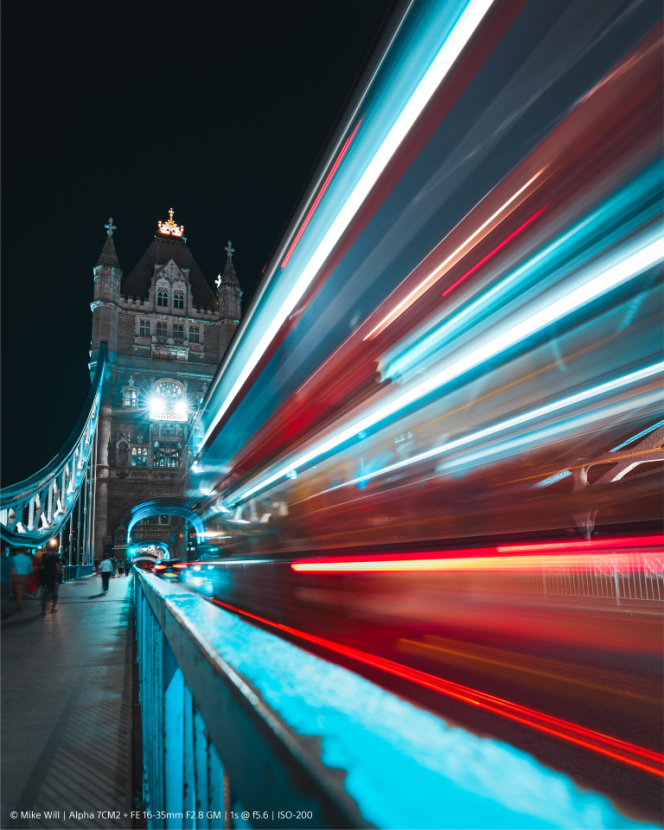 Lunga esposizione del Tower Bridge con scie luminose dei veicoli di passaggio di notte. Tonalità blu e arancioni.