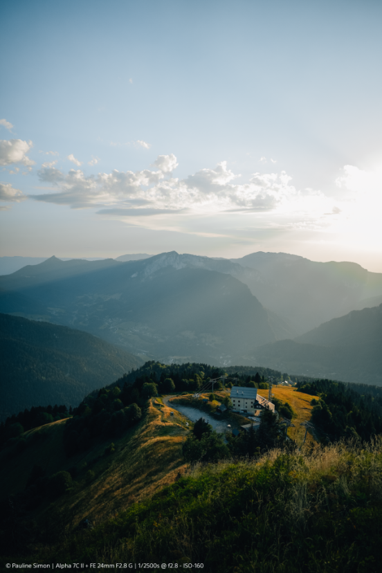 Una scena di montagna al tramonto con un edificio in cima a una collina e montagne sullo sfondo.