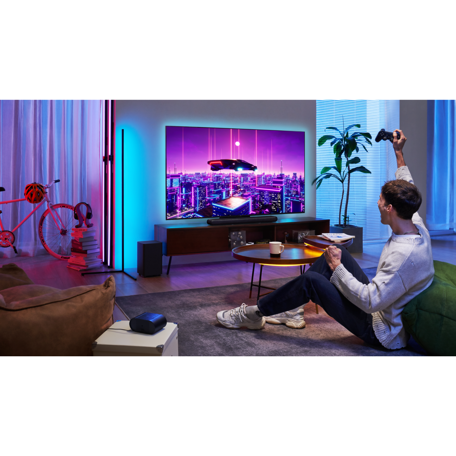 A man plays a video game on a large TV. The room has colorful lighting.