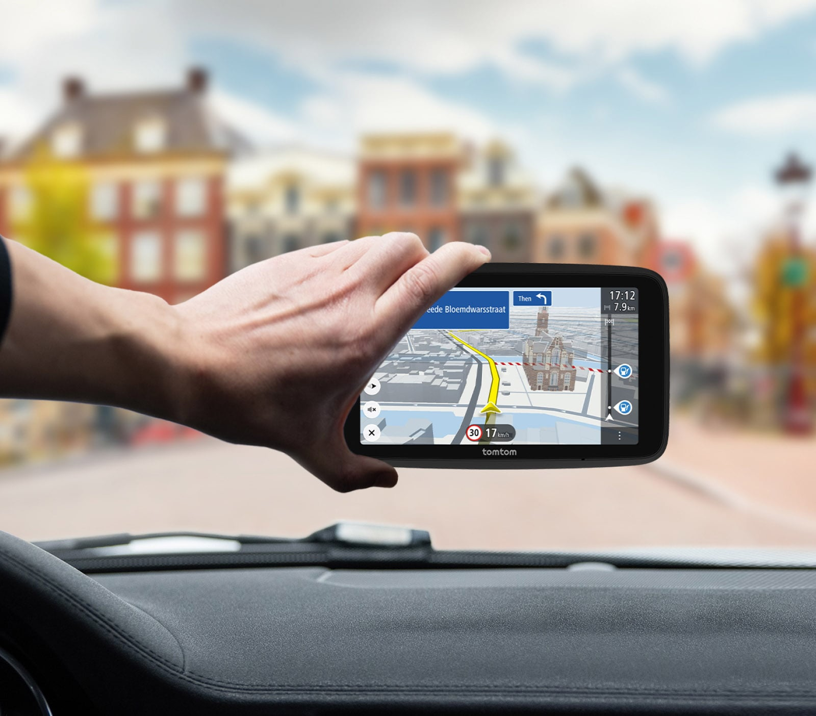 Eine Hand hält ein TomTom GPS-Gerät, das eine Karte mit Navigationsanweisungen auf dem Armaturenbrett zeigt.