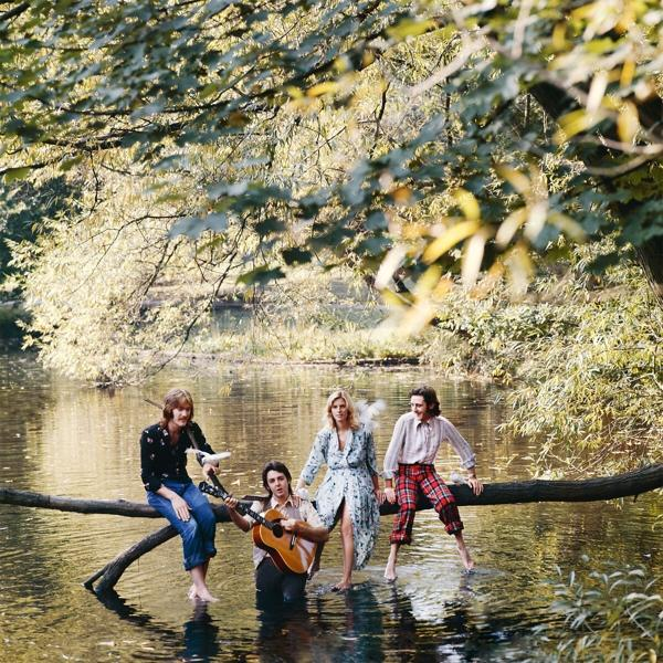 A Beatles egy tóban. Egy farönkön ülnek és a vízben. Fák a háttérben.