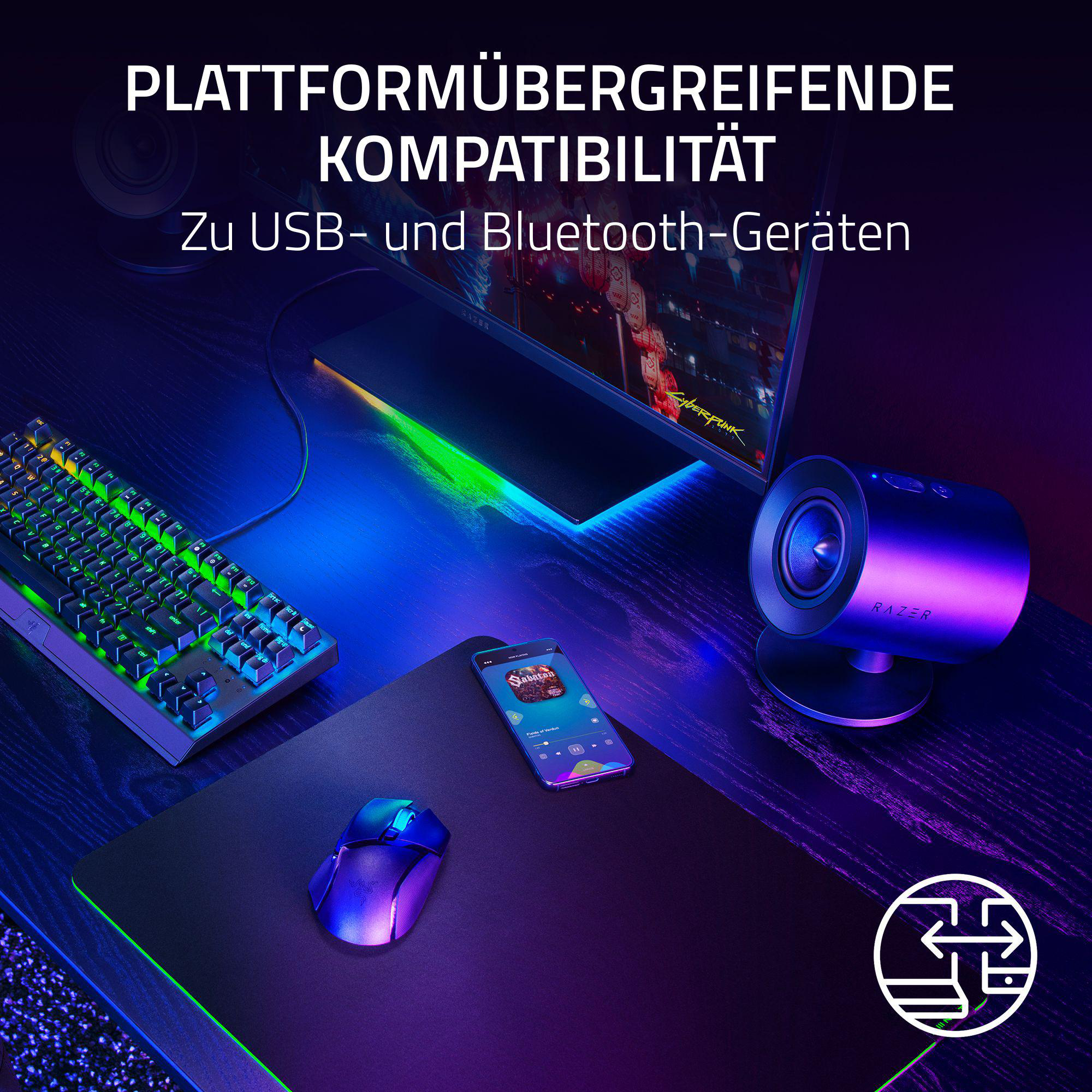 Ein Schreibtisch-Setup mit Tastatur, Maus, Lautsprecher und Smartphone. Ein Monitor zeigt das Spiel 'Cyberpunk'.