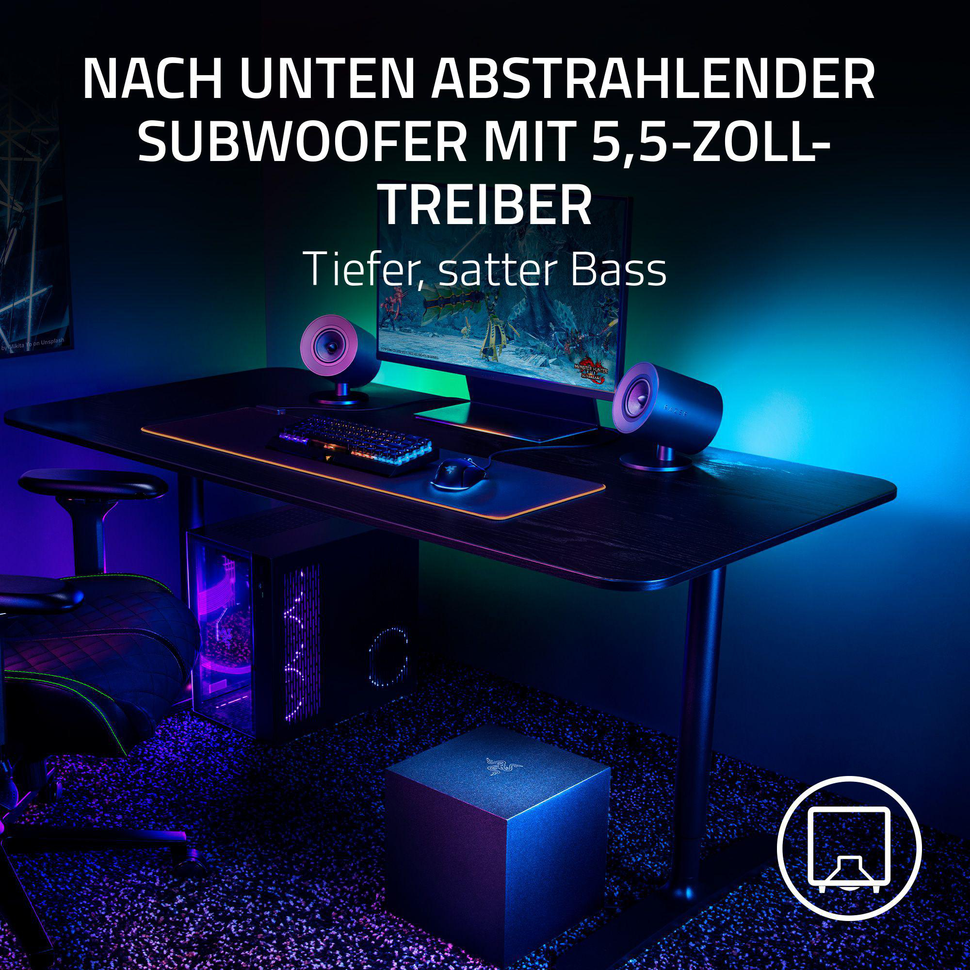 Ein Gaming-Setup mit Lautsprechern, Monitor, Tastatur und Subwoofer auf einem schwarzen Schreibtisch.
