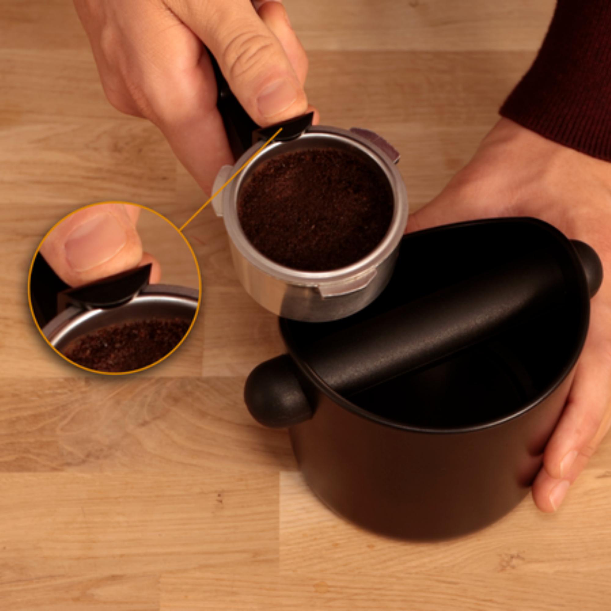 Hände halten einen Siebträger mit Kaffeepulver, neben einer schwarzen Abschlagbox.