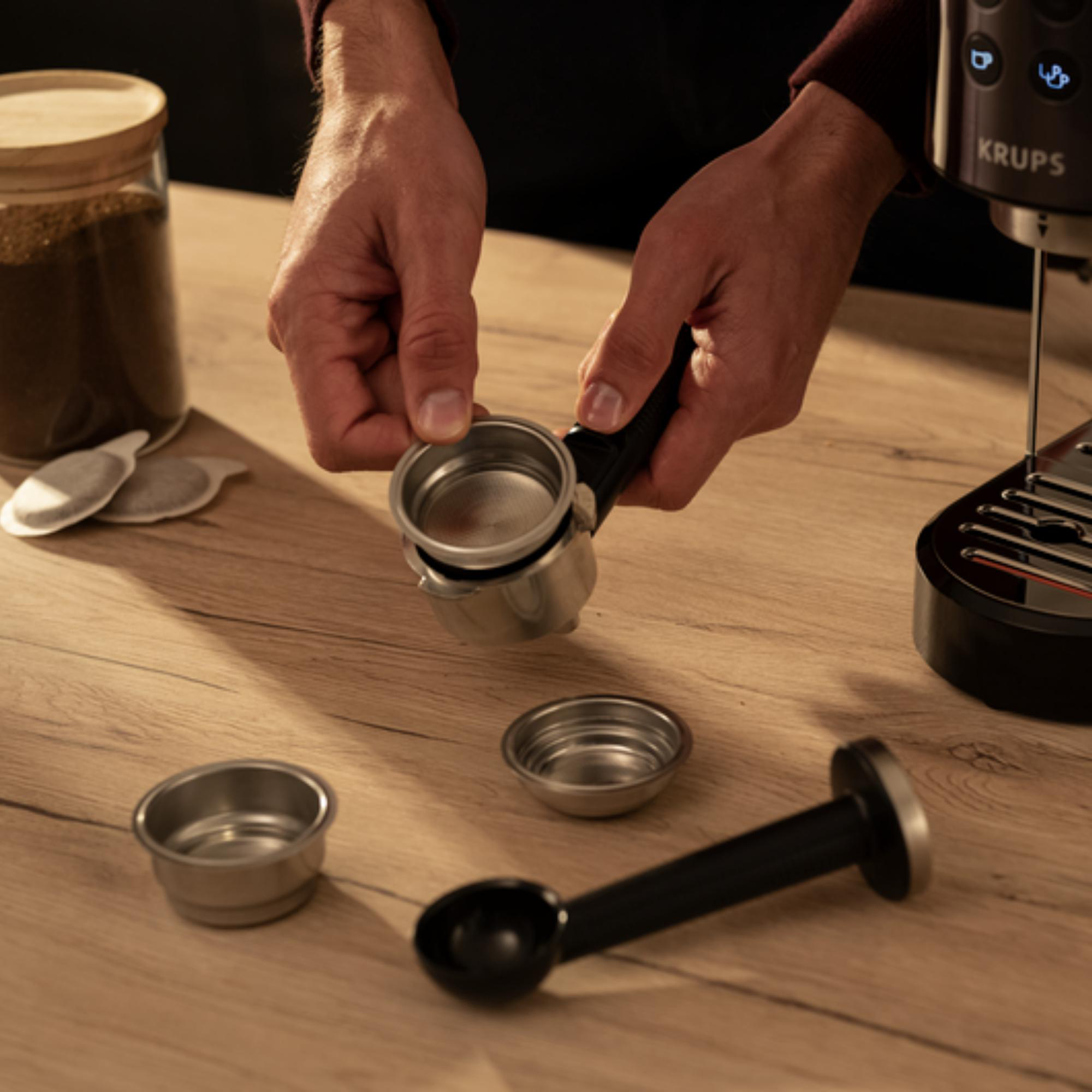 Hände, die die Teile einer Espressomaschine auf einem Holztisch zusammenbauen.