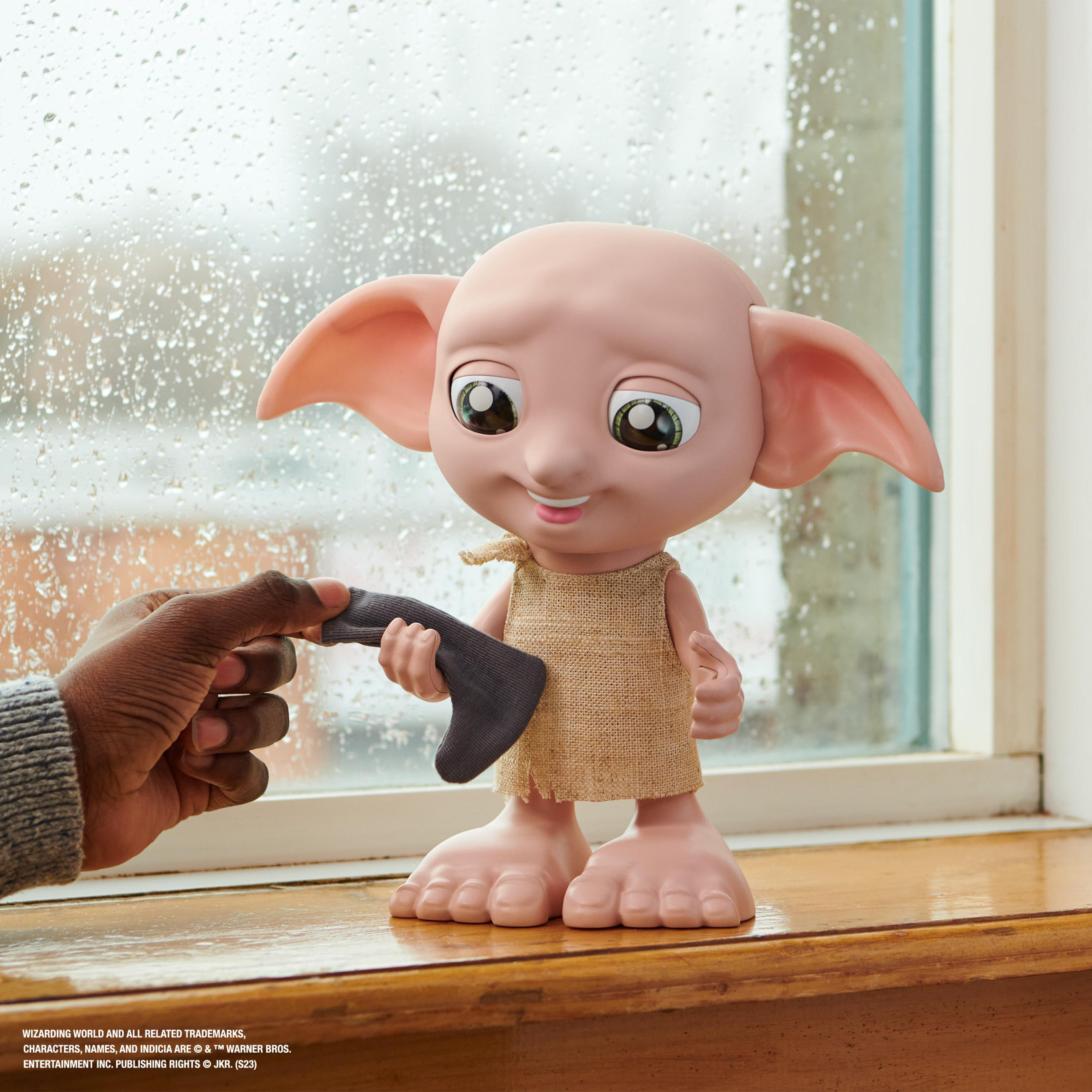 Dobby-Puppe. Die Hand einer Person hält eine Socke. Fenster im Hintergrund.