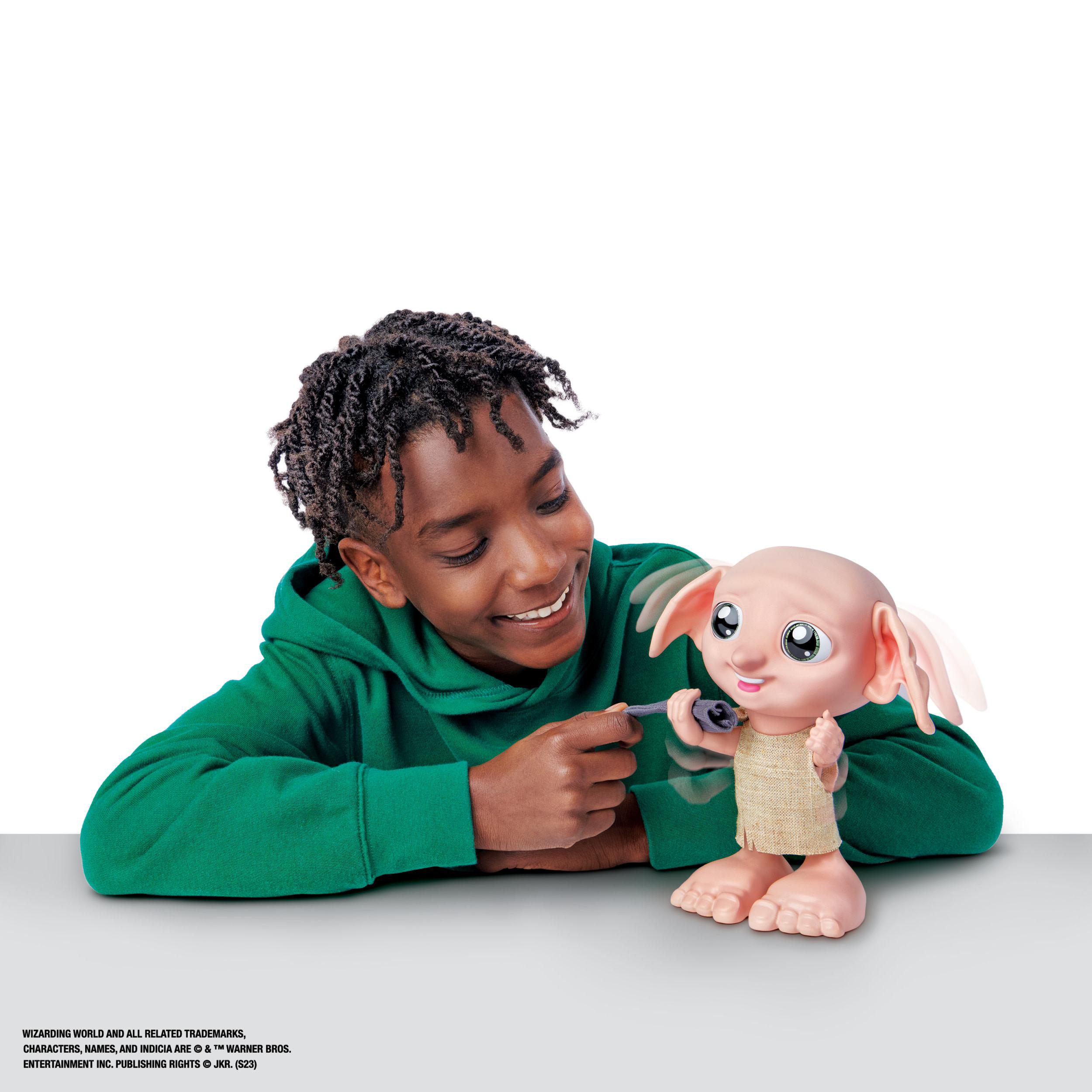 Ein Junge mit grünem Hemd betrachtet eine Dobby-Puppe, die ein kleines Objekt hält.