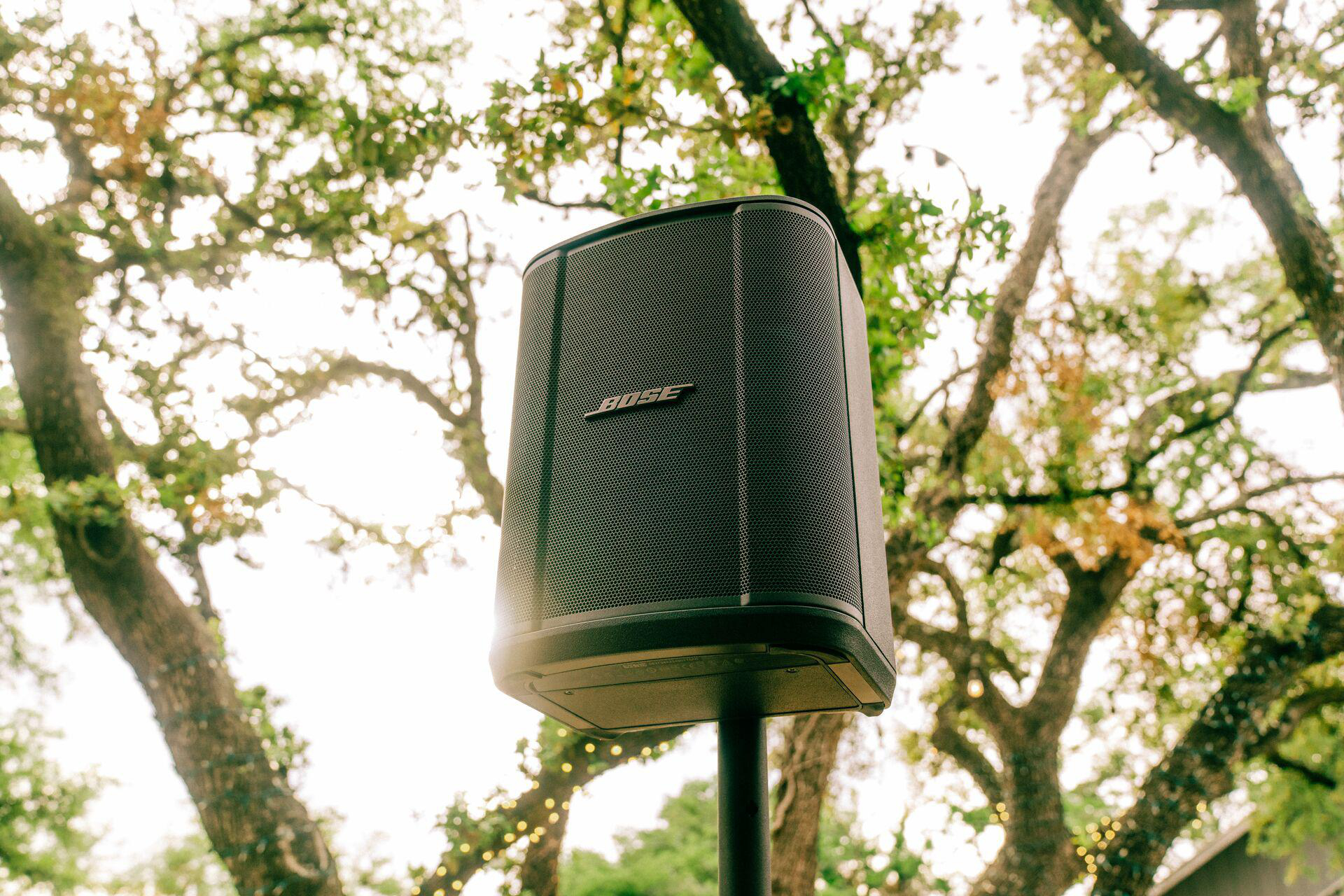 Schwarzer Bose-Lautsprecher auf einem Ständer zwischen Bäumen.