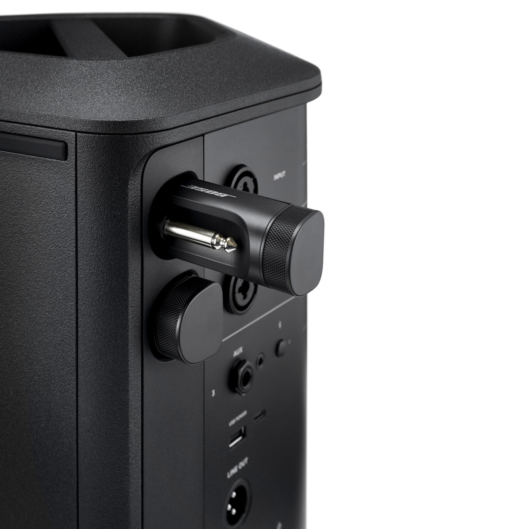 Ein schwarzer Lautsprecher mit eingesteckter Buchse und Anschlüssen. Das Gerät befindet sich auf weißem Hintergrund.