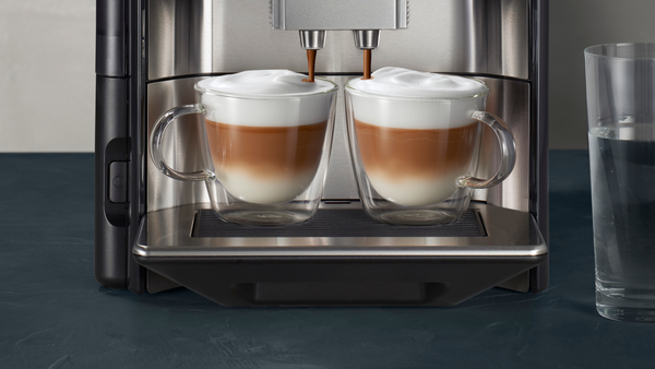 Espresso makinesi, süt ve köpükle dolu iki bardak bardağa kahve döküyor.