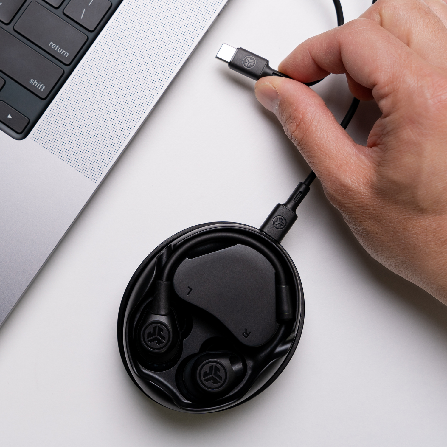 Zwarte oortelefoons in een zwart etui aangesloten op een laptop via USB-C. Witte achtergrond.