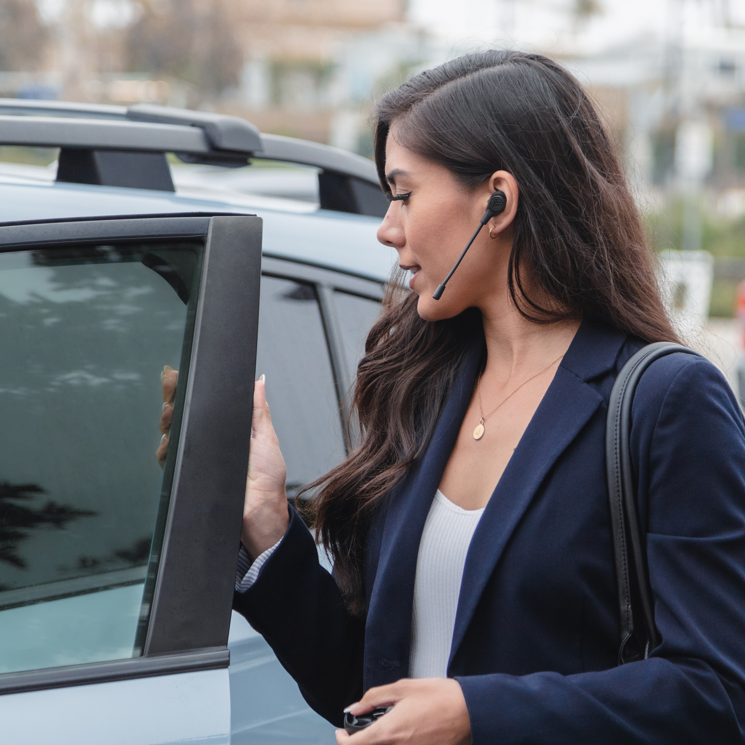 Vrouw die een autodeur opent, met een headset. Blauwe auto, buitenomgeving.